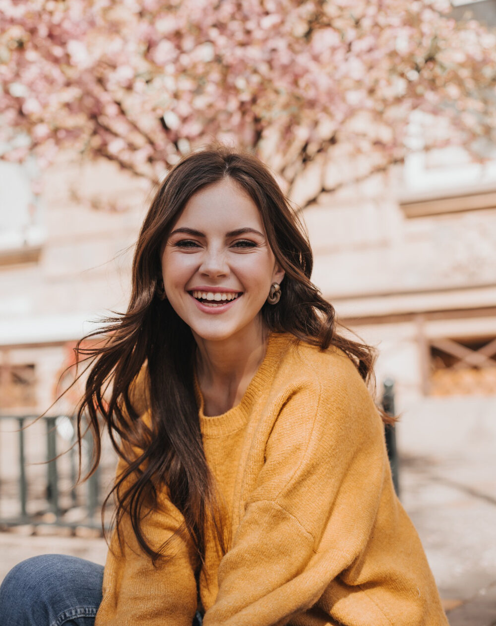 cheerful girl cashmere sweater laughs against backdrop blossoming sakura portrait woman yellow hoodie city spring e1687250504881